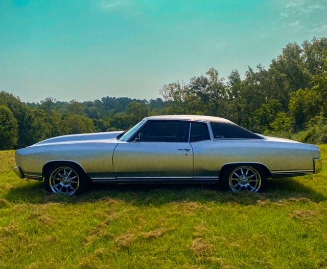 A silver car is parked in a grassy field.