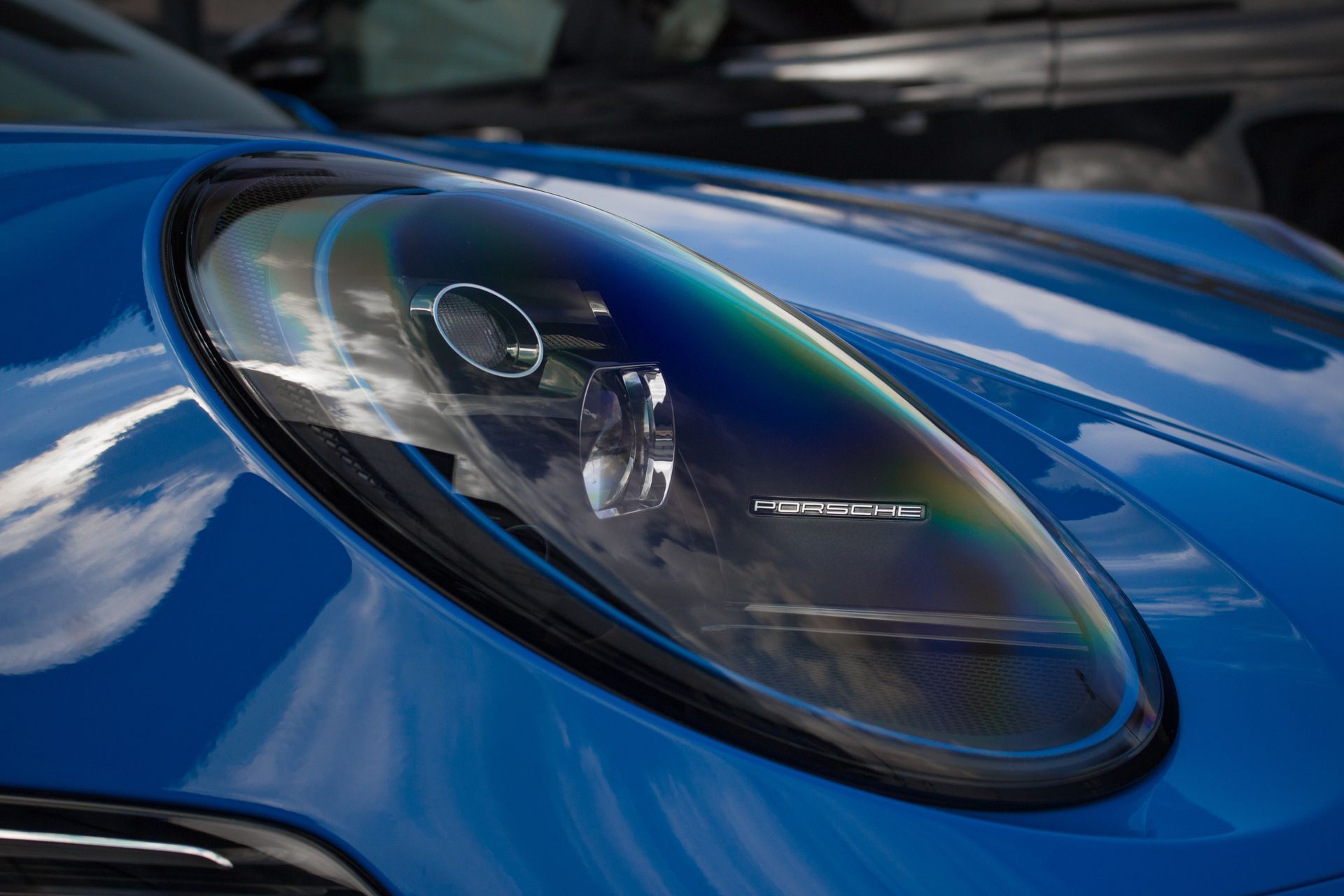 Close-up of a blue sports car headlight reflecting the sky and surrounding objects.
