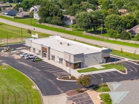 Aerial view of a small office building with parking lot and grassy roadside area.