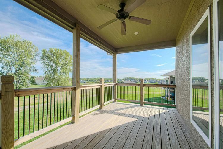 Covered back porch with wooden deck, railing, ceiling fan, and view of a grassy yard and neighboring houses.