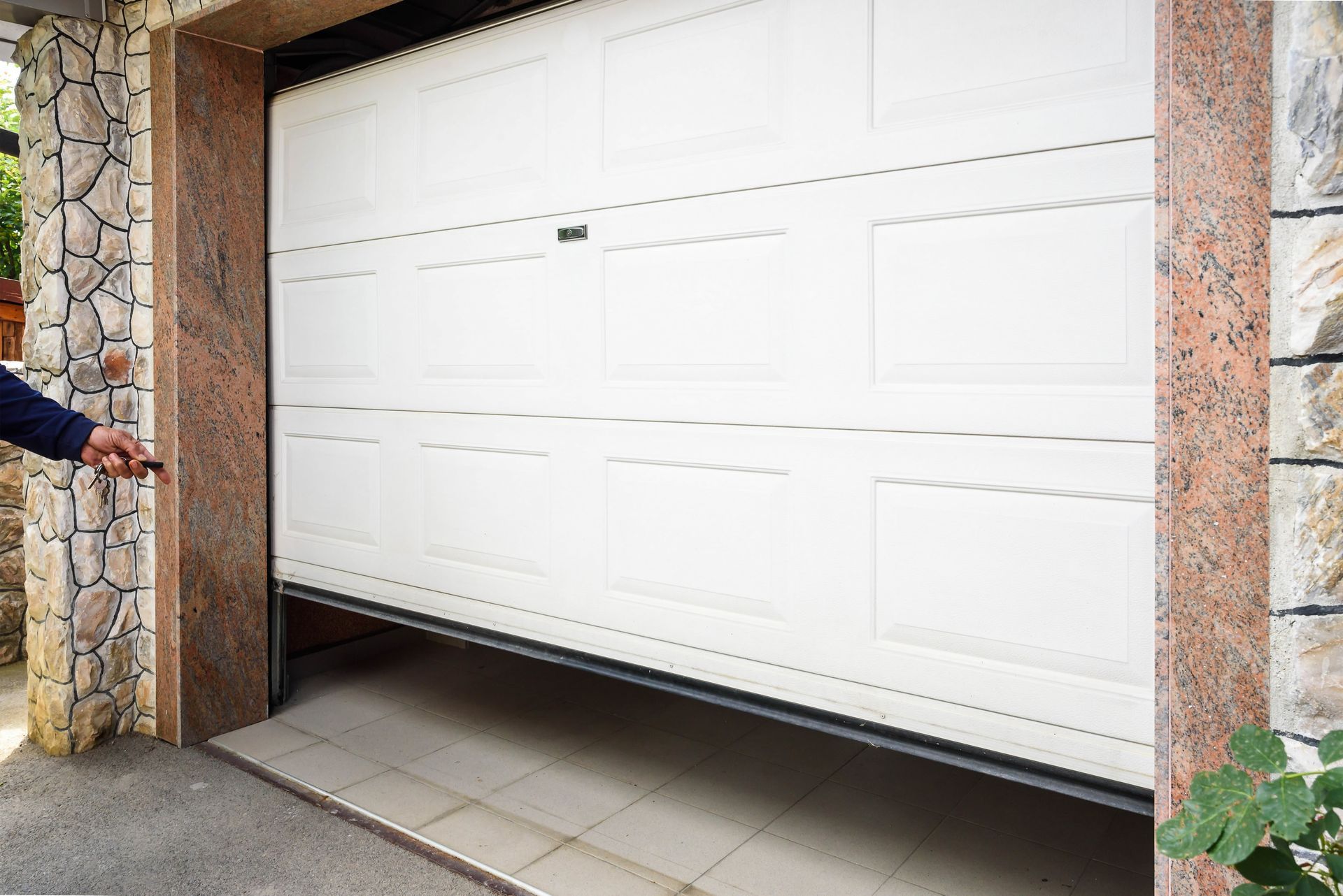 A man is opening a white garage door with a key.