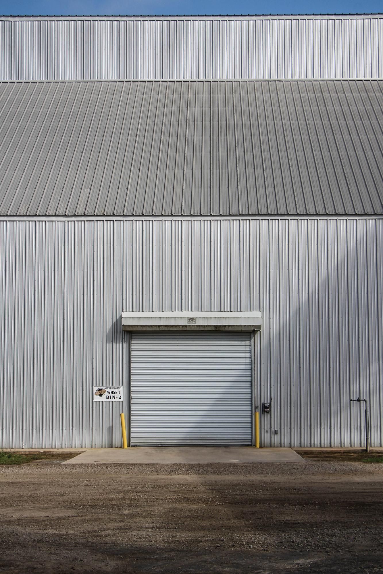 A large white building with a garage door and a blue sky in the background. Commercial garage door replacement