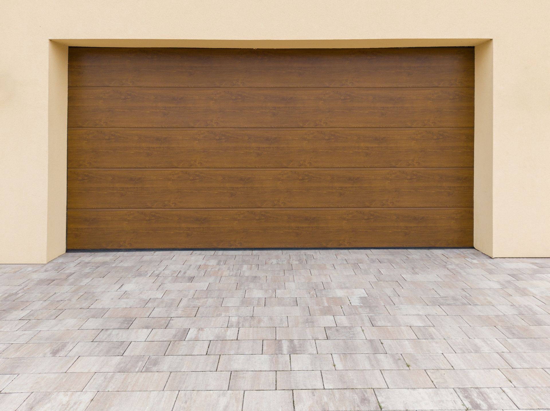 A wooden garage door with a brick driveway in front of it