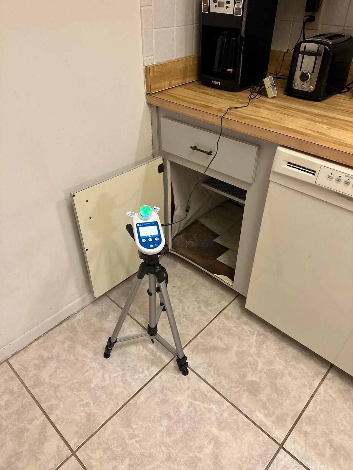 A tripod is sitting in a kitchen next to an open cabinet.