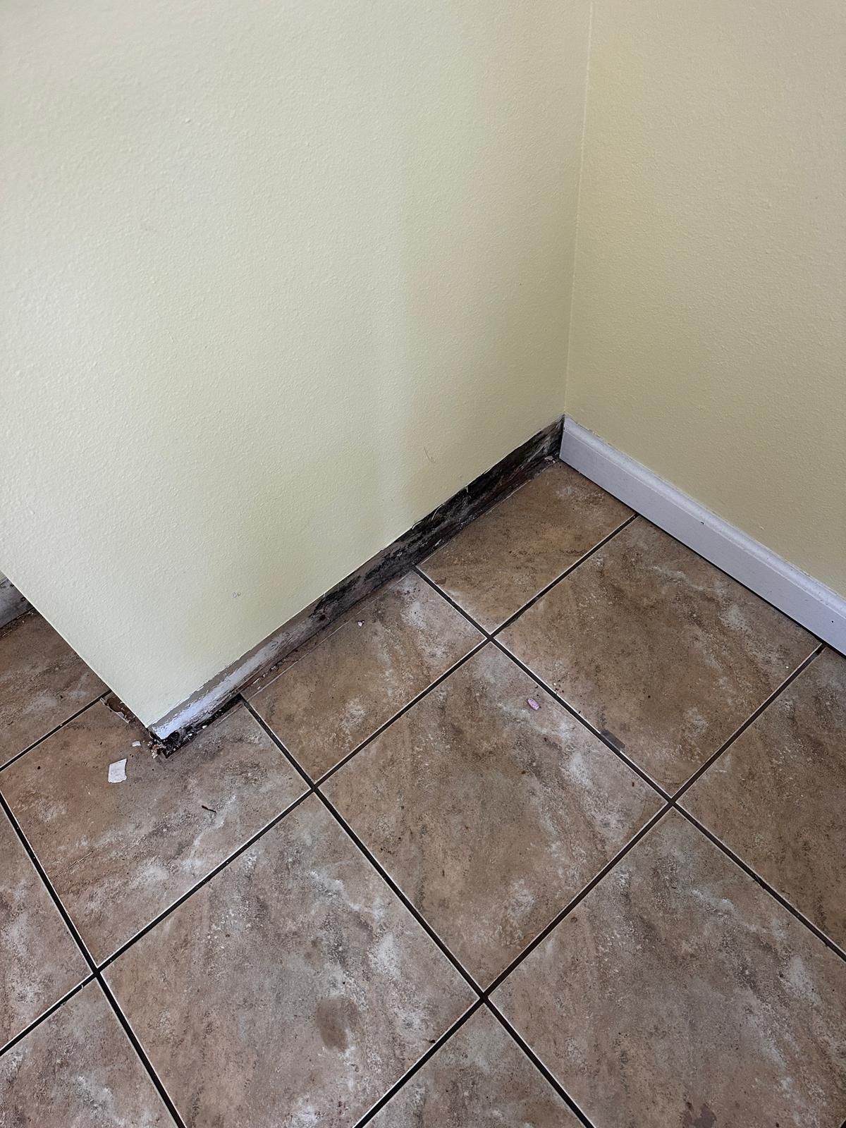 A corner of a room with tile floors and a yellow wall.