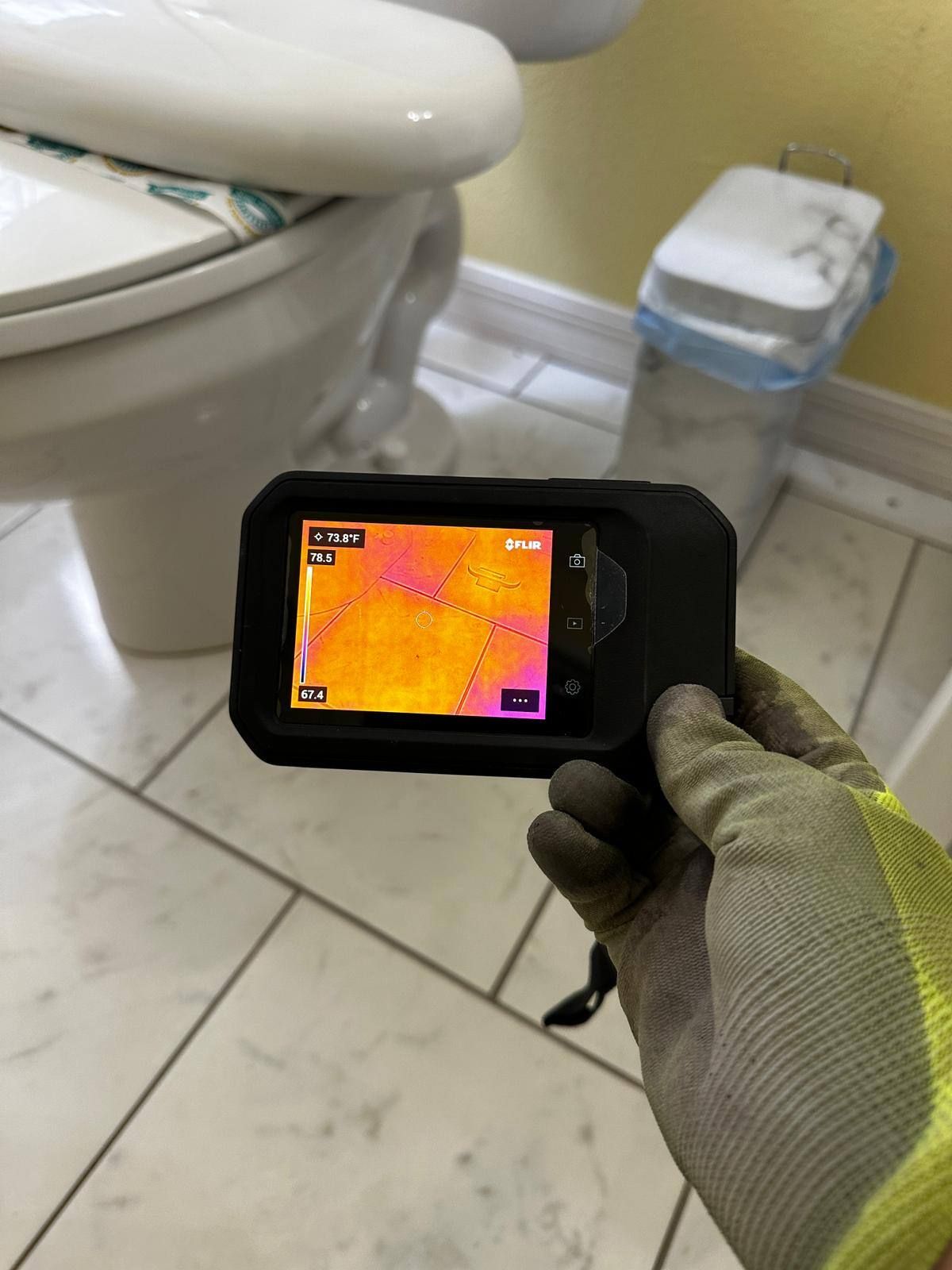 A person is holding a thermal camera in front of a toilet.