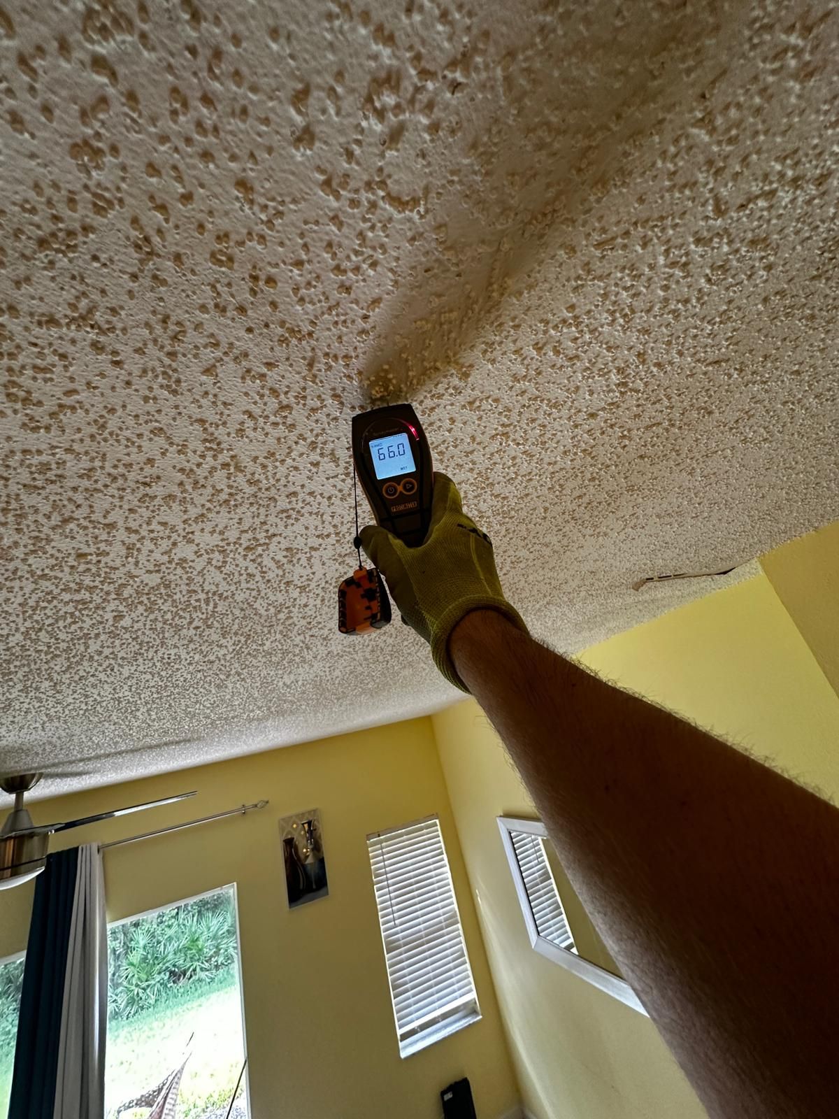 A person is measuring the temperature of a ceiling with a thermometer.