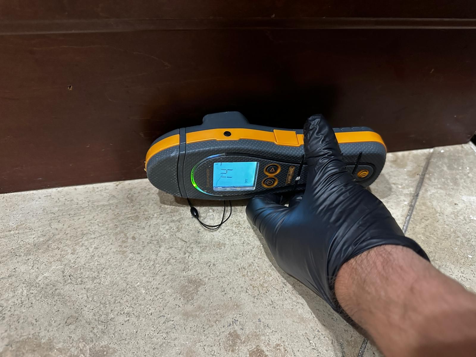 A person wearing black gloves is using a device on a tile floor.