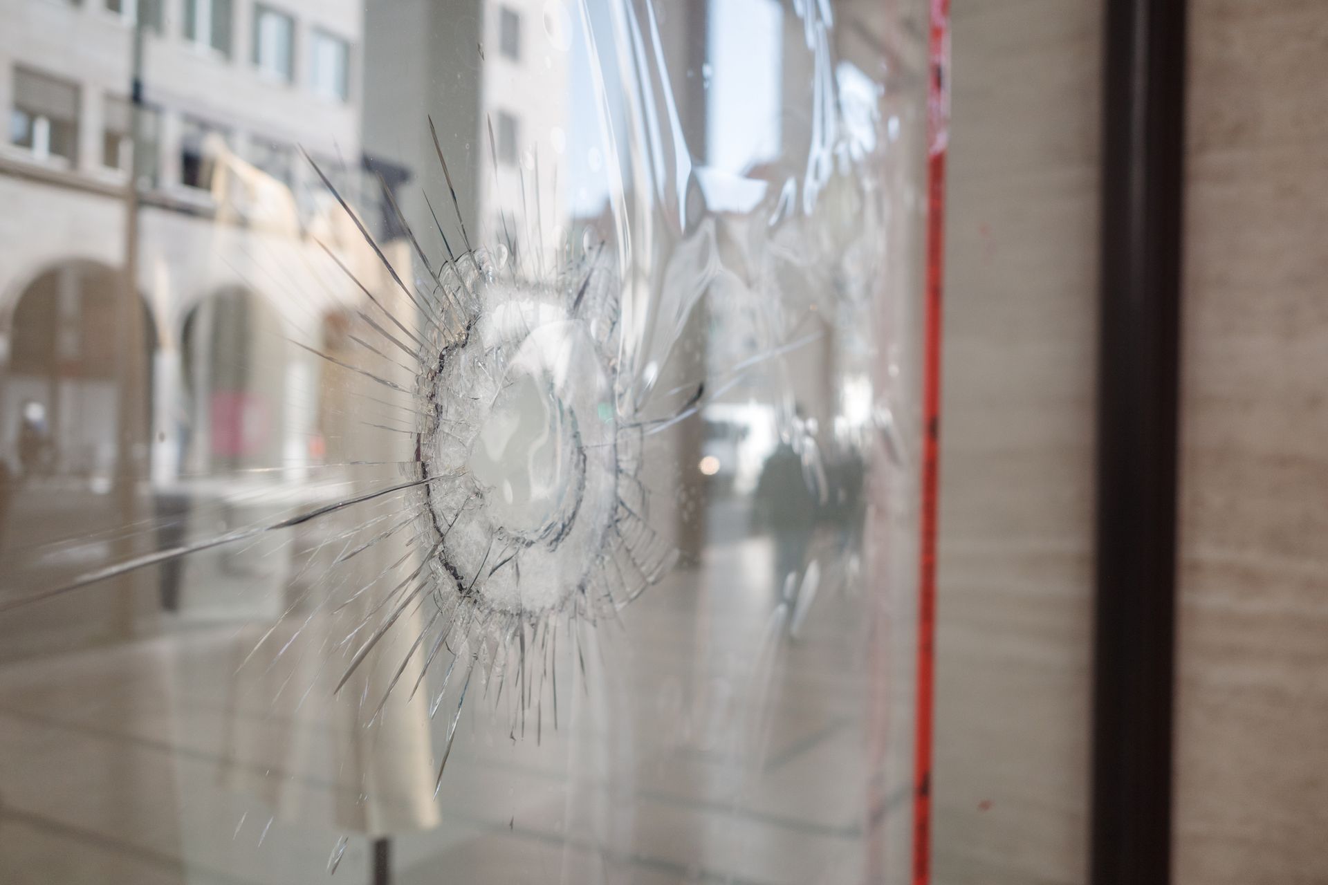 Close-up of cracked storefront window with central impact point.