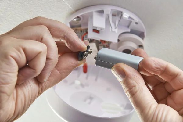 A person is removing a battery from a smoke detector.