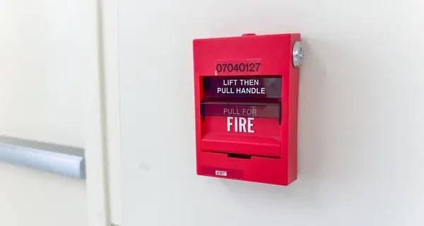 A red fire alarm is hanging on a white wall.