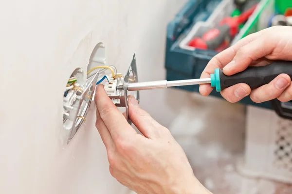 A person is fixing a light switch with a screwdriver.