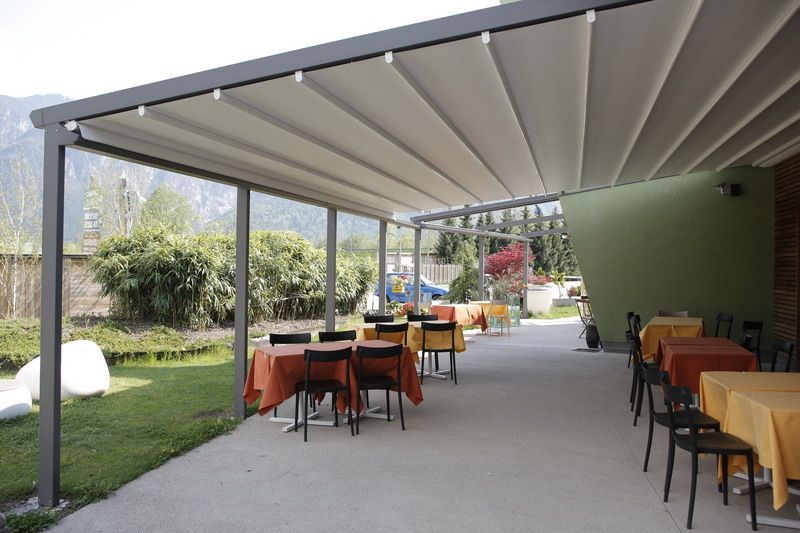 Outdoor patio with tables and chairs under a retractable awning. Green lawn and trees in the background.