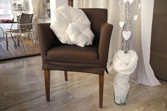 Brown armchair with white pillows, next to a vase with branches and heart decorations.