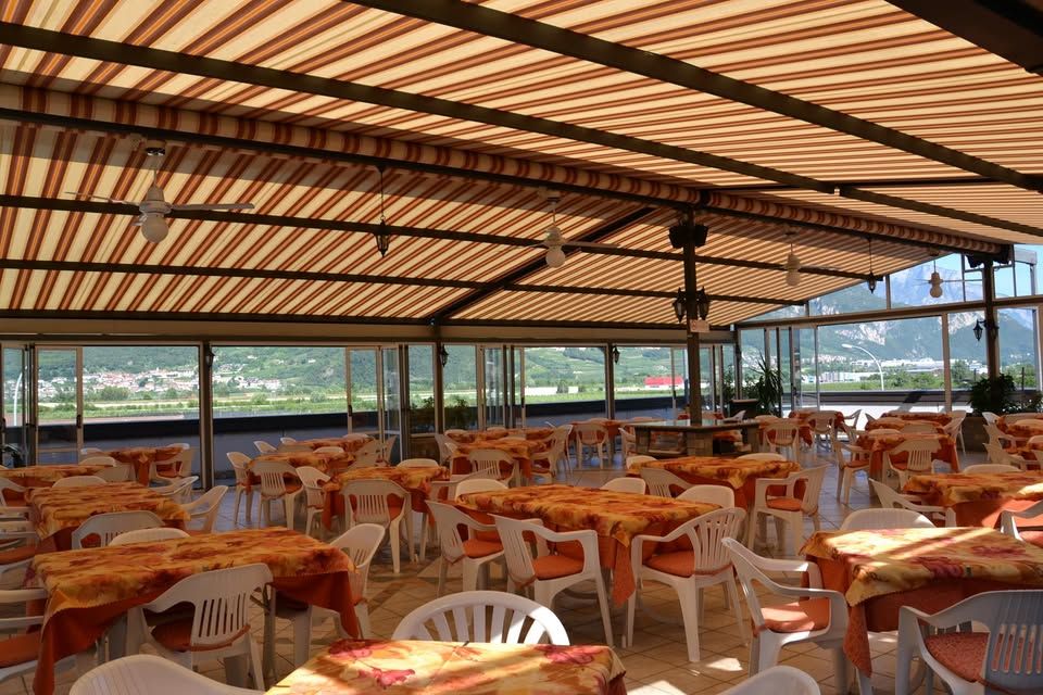 Covered outdoor dining area with tables, chairs, and striped awning. View of a town in the distance.