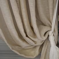 Beige linen curtain draped with white rope and tassel.