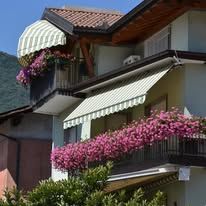 Balconies with awnings, overflowing with vibrant pink flowers. A building with a brown roof.