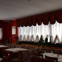 Restaurant interior with tables, dark red curtains, and white sheers.