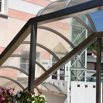 Black metal archway with curved glass roof panels, over an exterior entry.