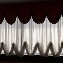 White sheer curtains beneath a dark valance, silhouetted against a bright window.