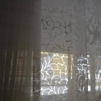 Close-up view of a sheer window covering with a floral pattern, allowing sunlight to filter through.