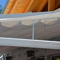 White awning with wooden roof beams, covering an outdoor seating area.