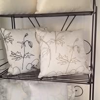 Two white pillows with black floral embroidery on a black metal shelf.
