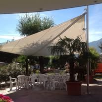 Large sun sail over patio with tables and chairs, palm tree in the foreground.
