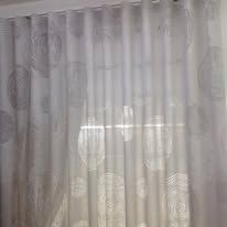 White sheer curtains with a repeating circular pattern, hanging in front of a window.