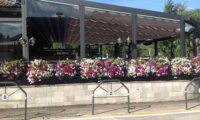 Restaurant with a retractable awning, stone facade, and a planter filled with colorful flowers.