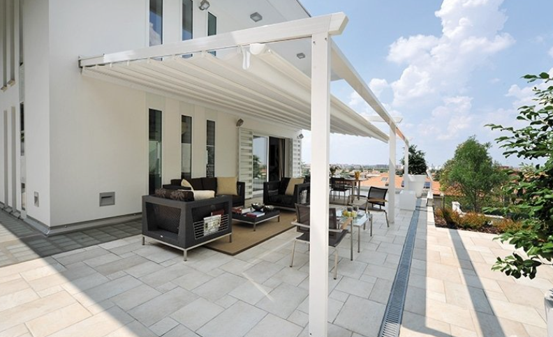 White pergola over patio with seating, overlooking city. Sunny day, modern architecture.
