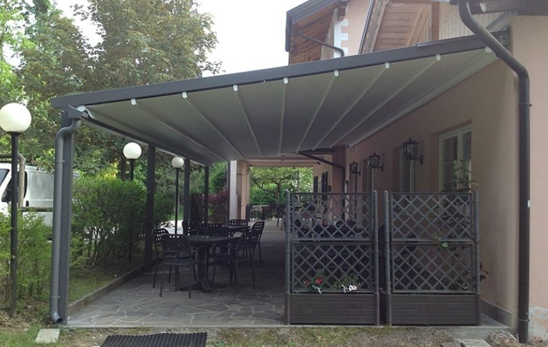 Patio with retractable gray awning over tables and chairs beside a building with decorative trellis.
