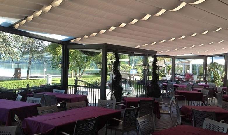 Outdoor dining area with tables and chairs under a retractable awning, trees in the background.