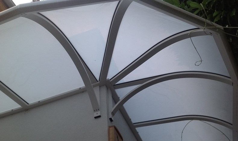 White arched awning with metal supports attached to a white wall.