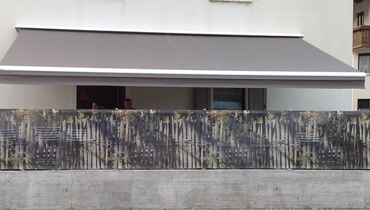 Gray retractable awning over a balcony with a weathered wooden fence in front.