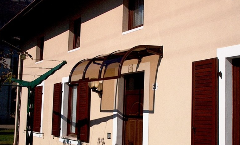 Tan house with brown shutters and a curved awning over the front door.