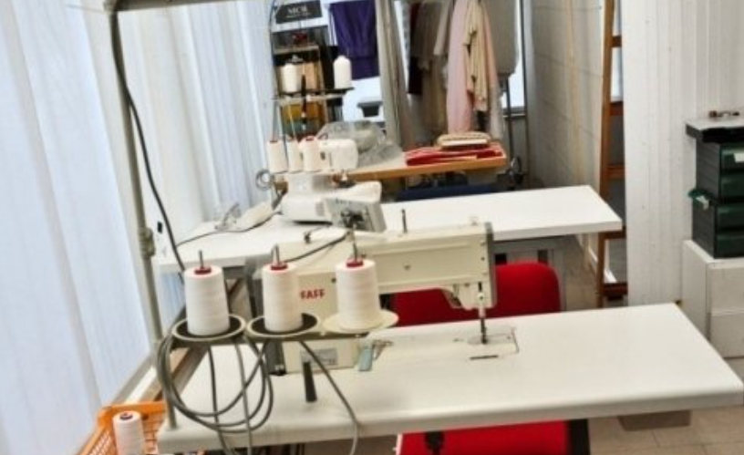 Sewing machines on white tables in a bright room. Spools of thread are visible.