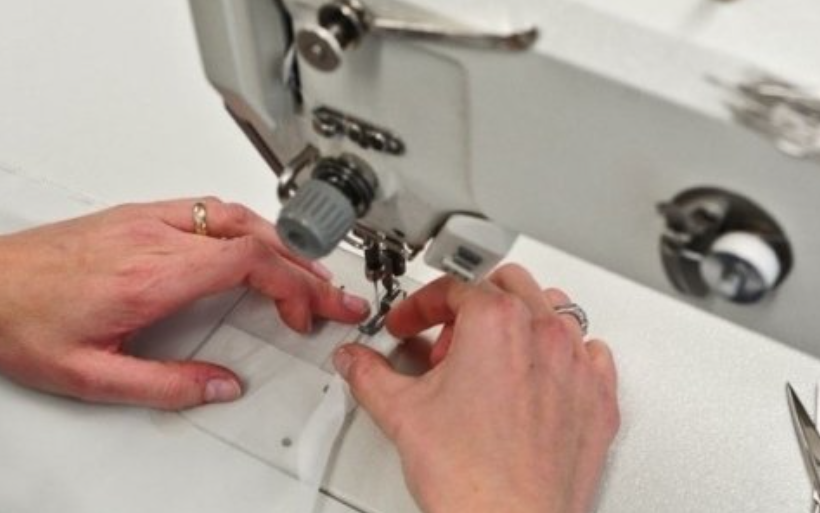 Hands sewing white fabric on a sewing machine.
