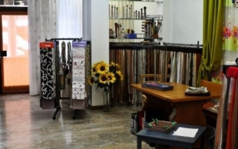 Interior of a fabric shop with curtains, samples, and a display of rods; table with samples, sunflowers.