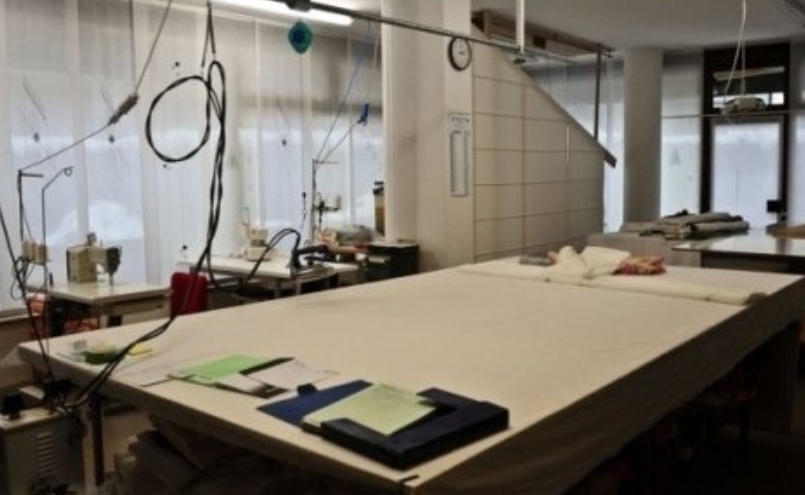 Sewing workshop interior with large cutting tables, sewing machines, and fabric rolls.