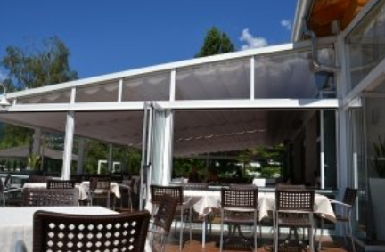 Outdoor restaurant seating area under a white canopy with tables and chairs, bright sunlight.