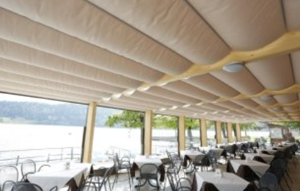 Restaurant patio with white-clothed tables, chairs, and a retractable beige awning overlooking a lake.