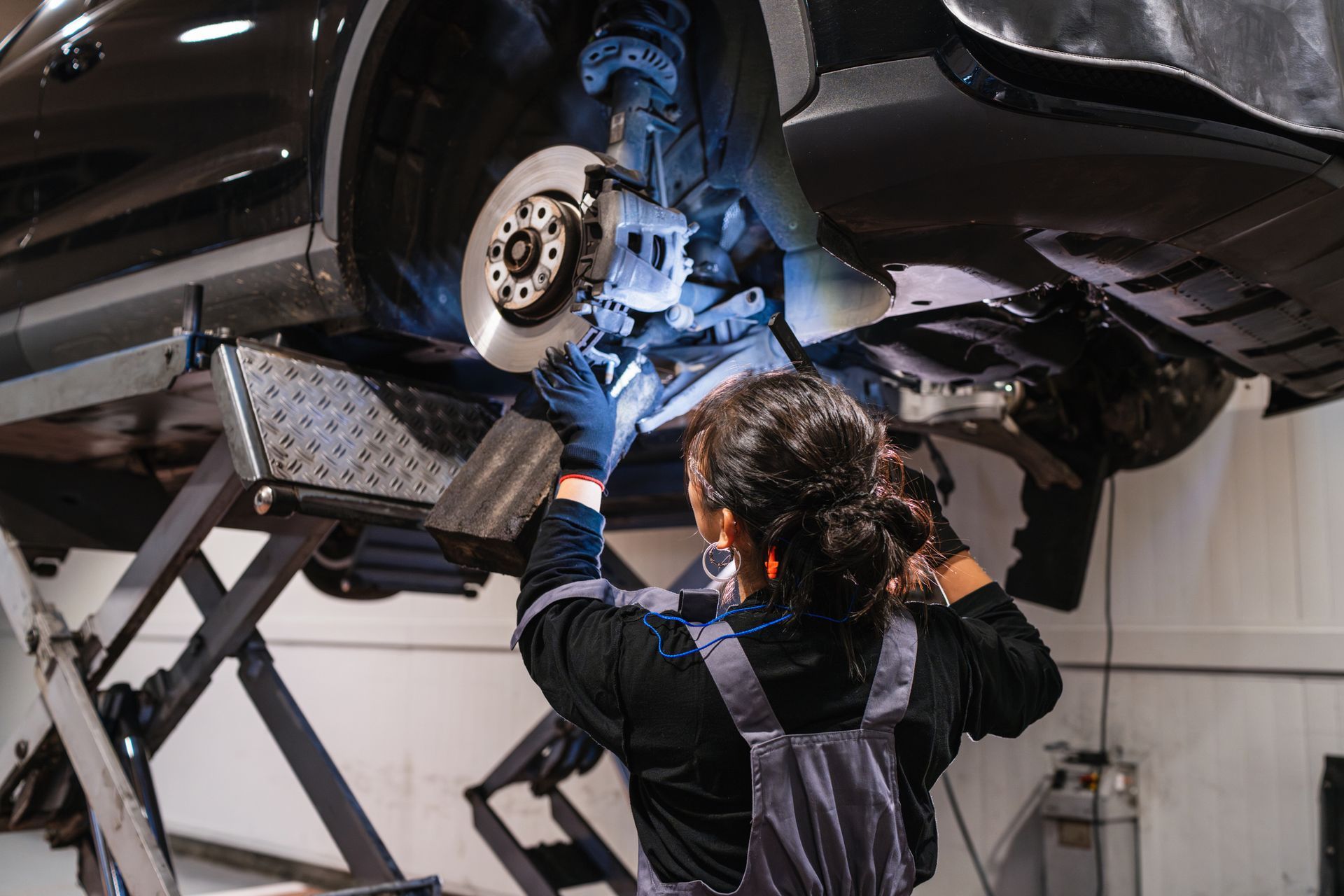 Mechanic working on car brakes; vehicle raised on a lift in a garage.