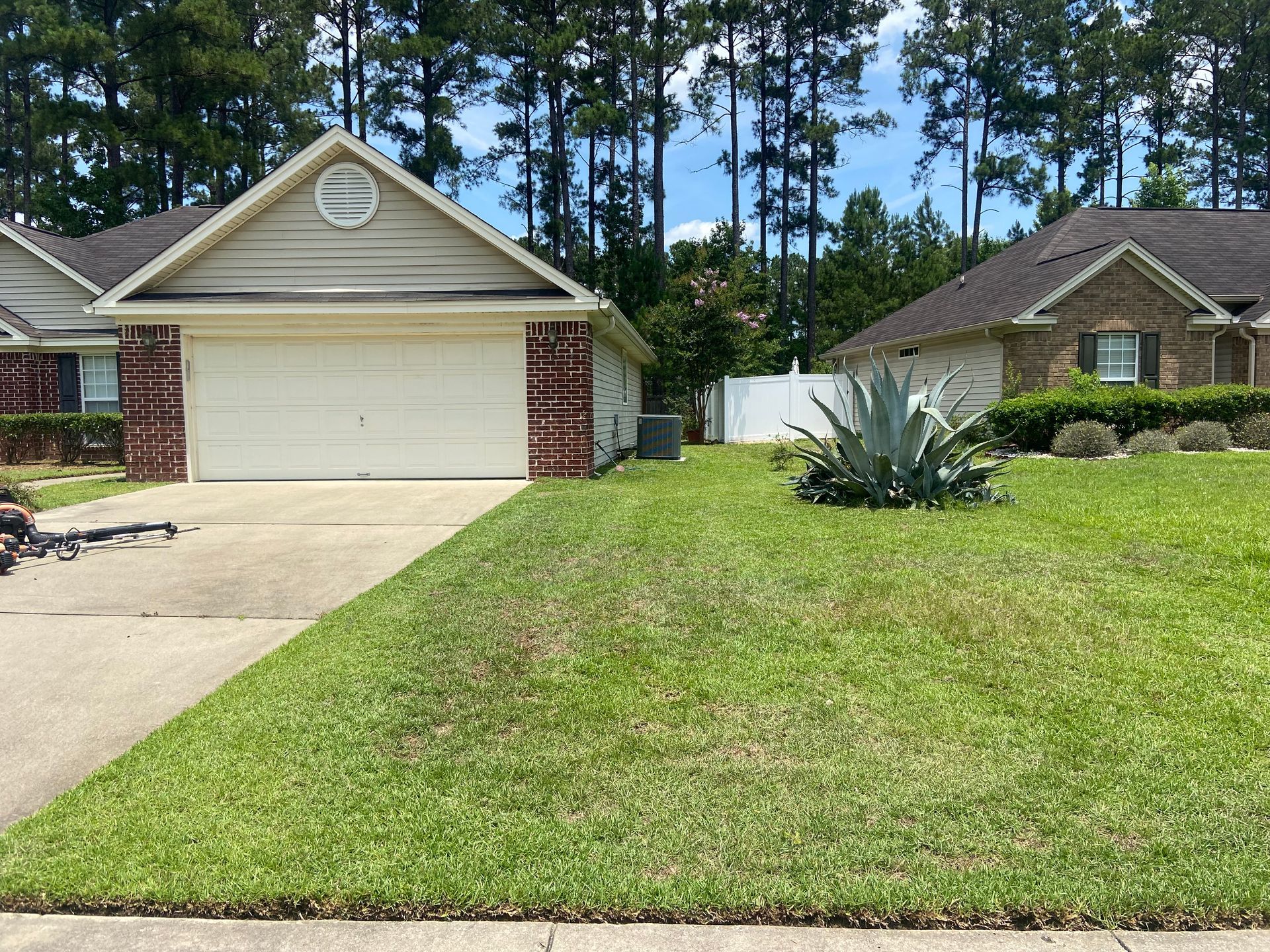 A lawn mower is cutting the grass in front of a house.
