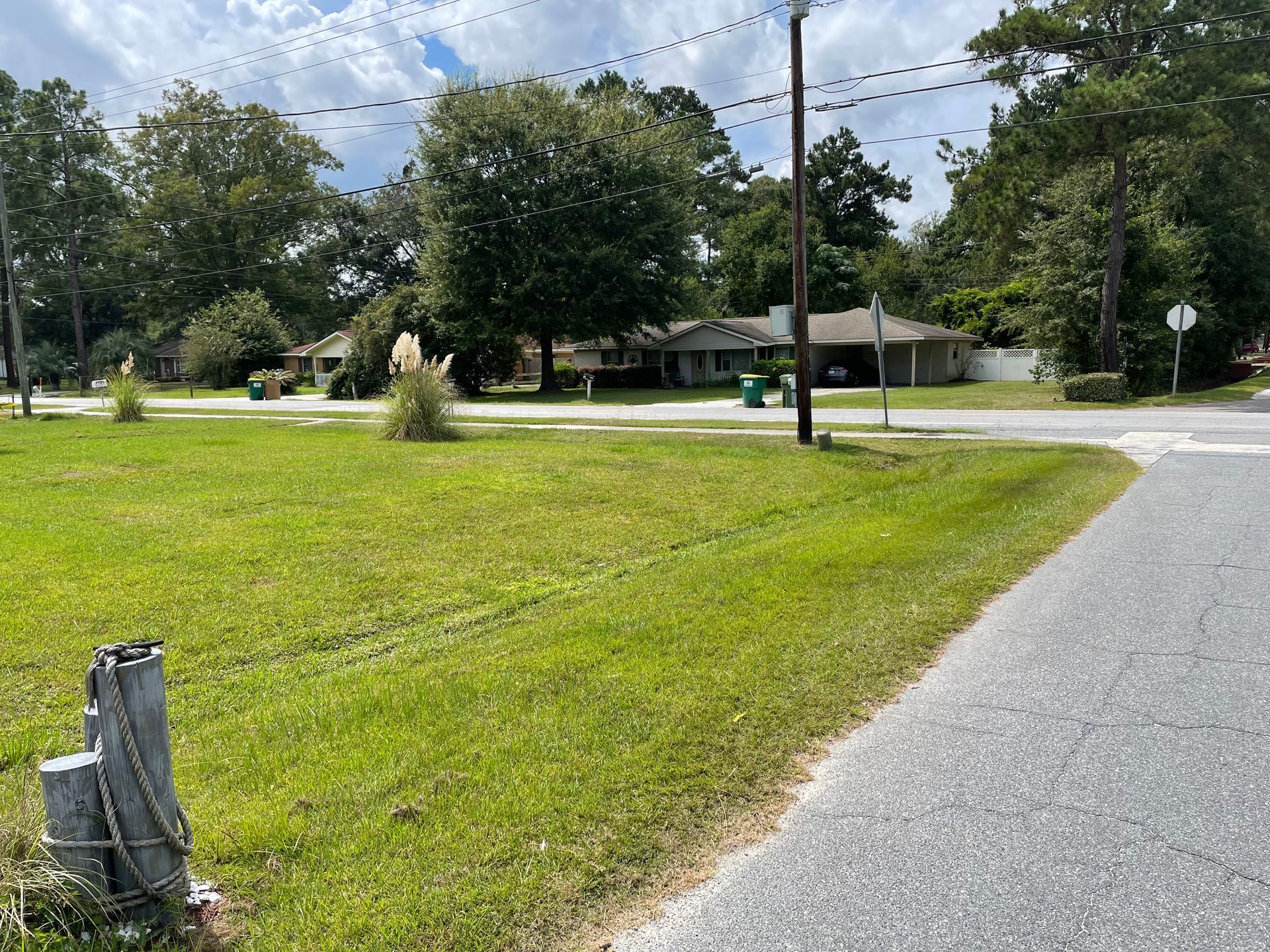 A grassy field next to a road with a house in the background.