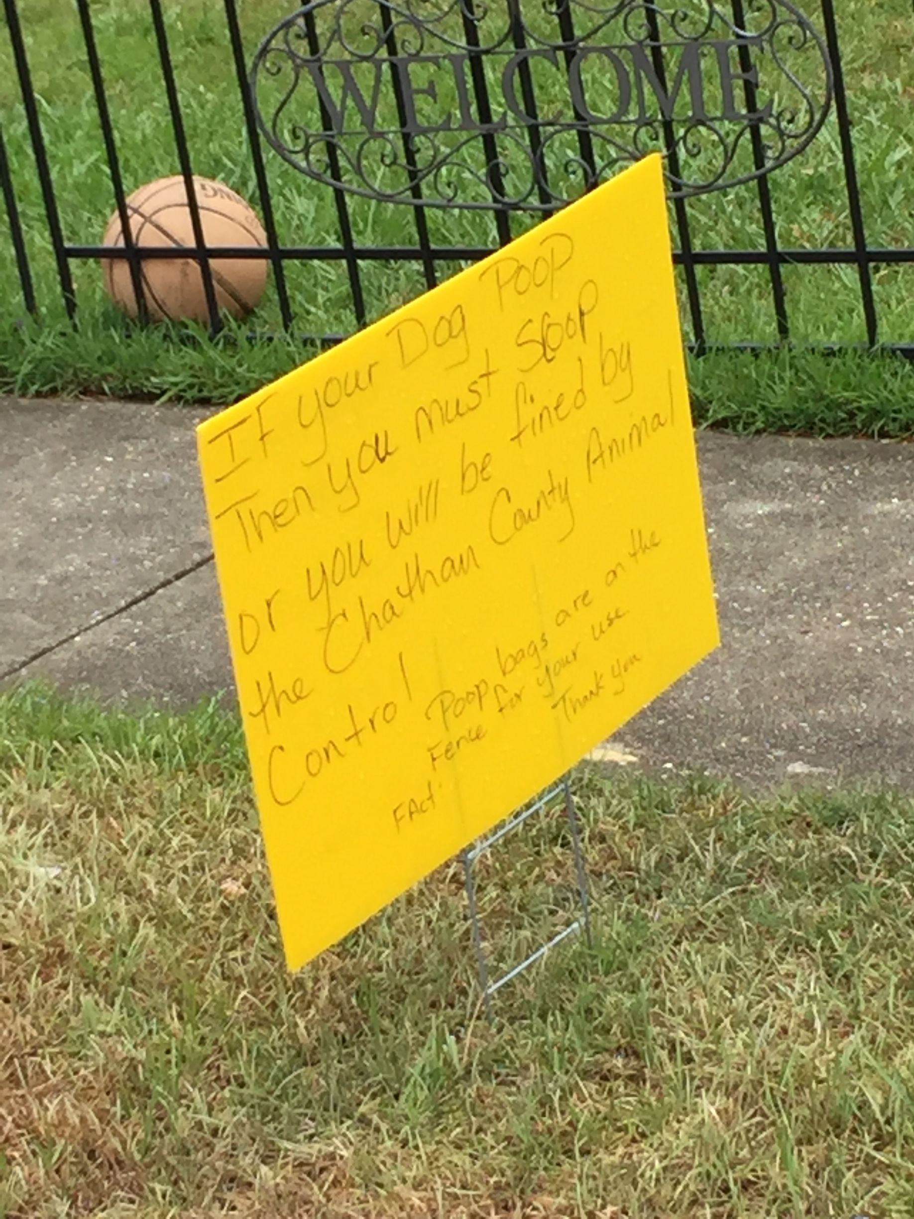 A yellow sign is sitting in the grass next to a basketball.