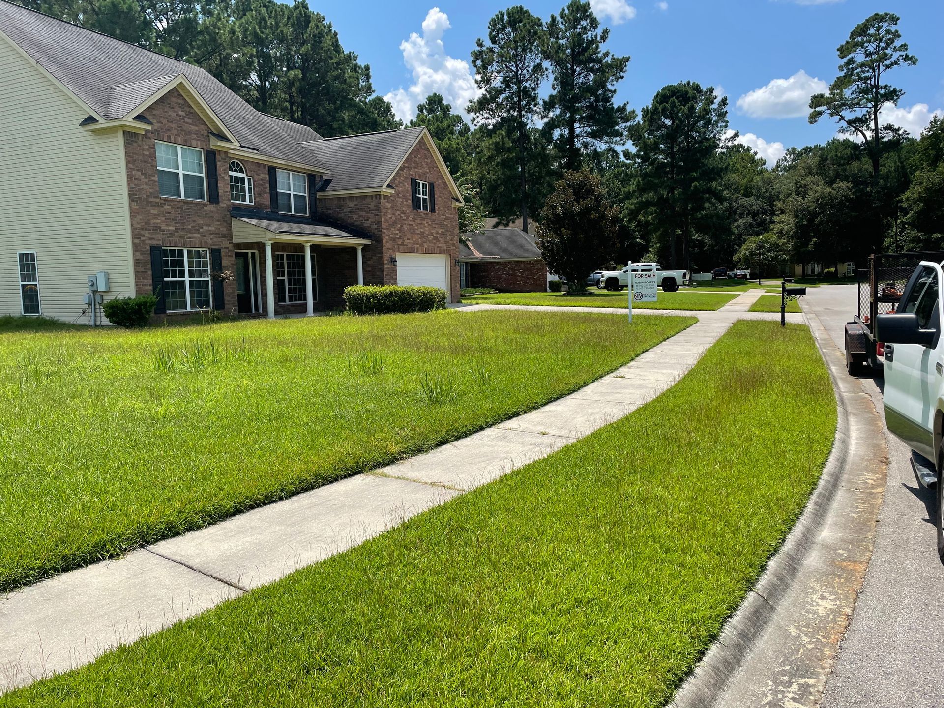 A white truck is parked on the side of the road in front of a brick house.