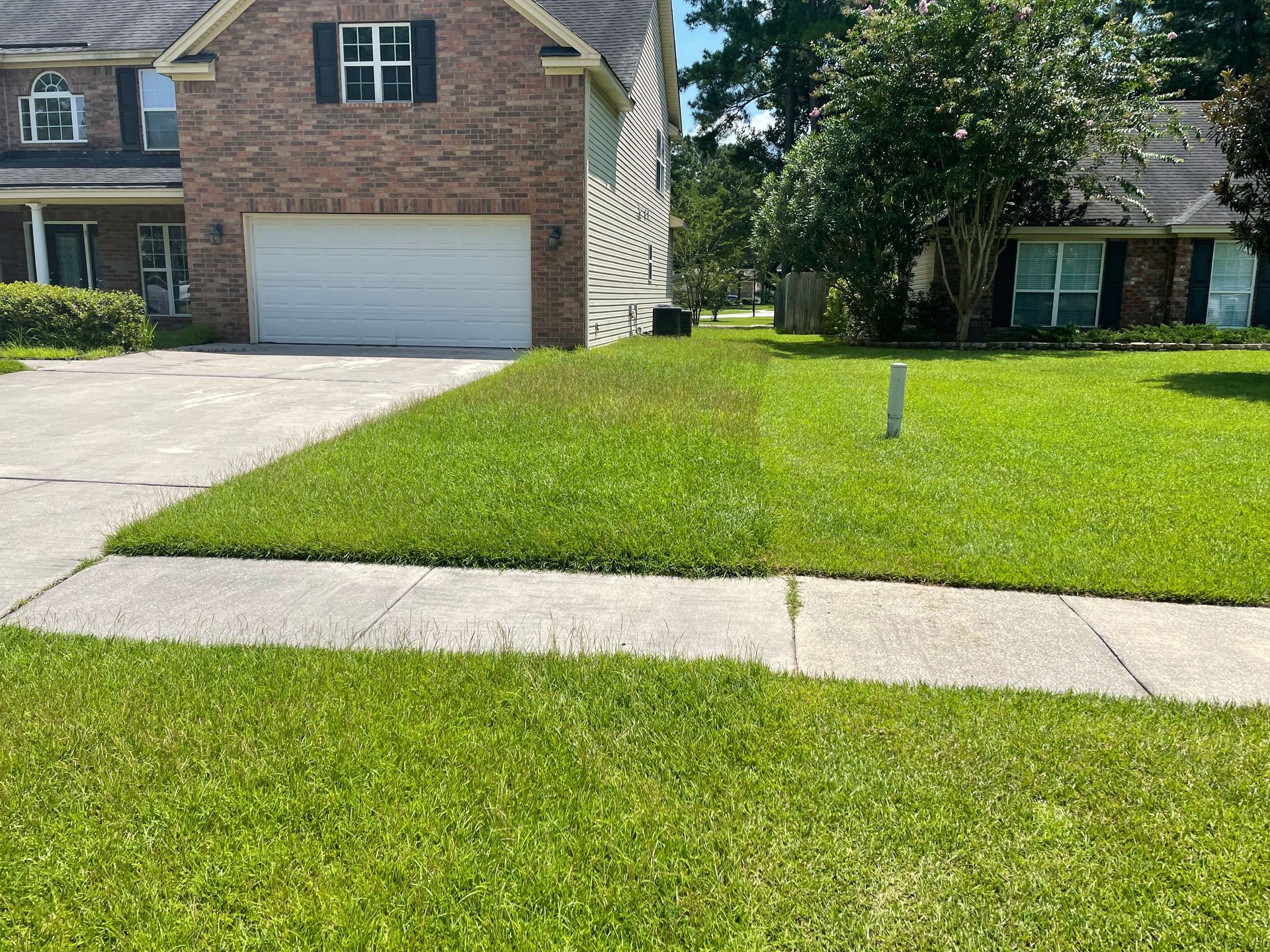 A brick house with a white garage door and a lush green lawn in front of it.