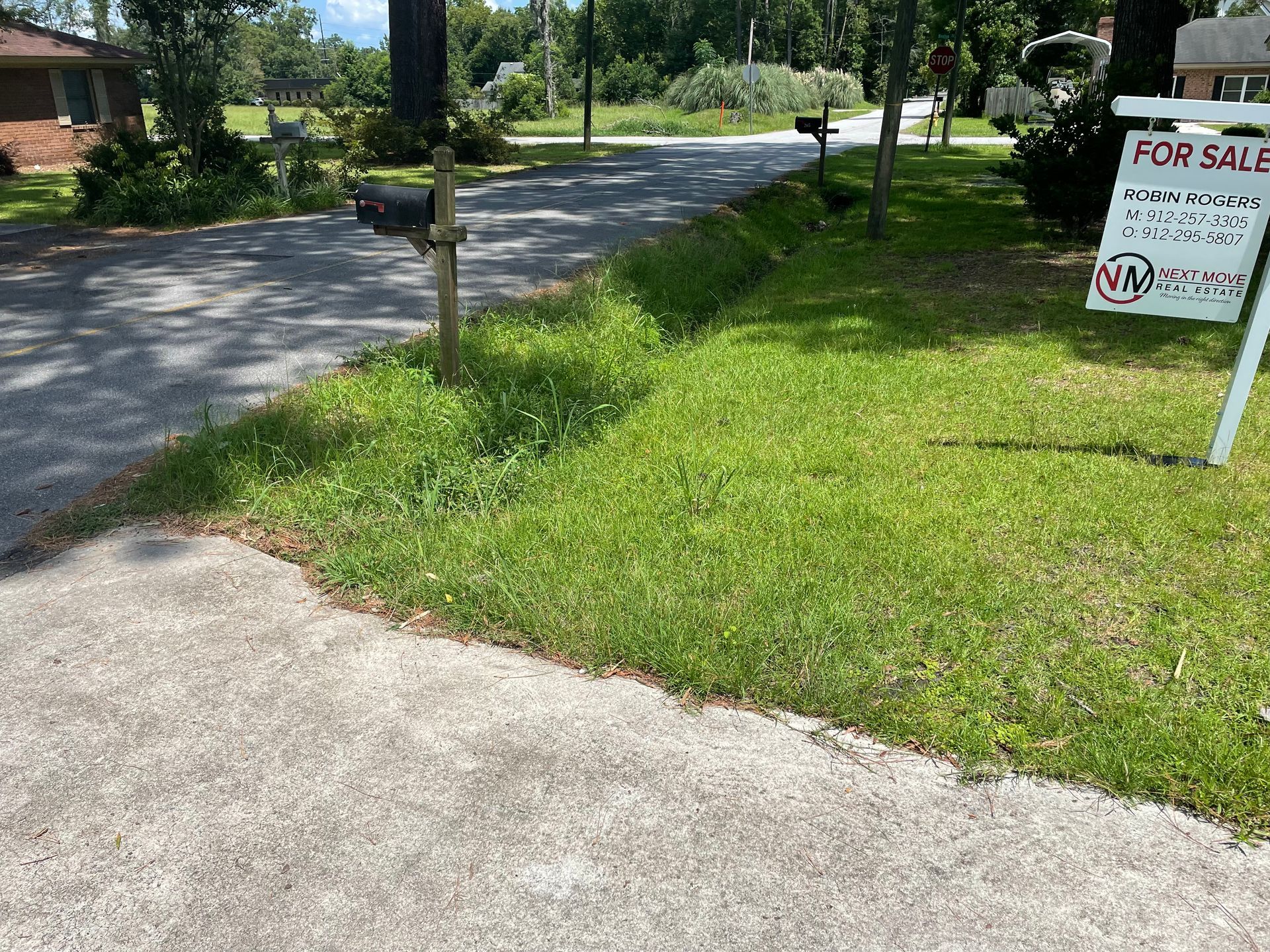 A for sale sign is sitting in the grass next to a driveway.