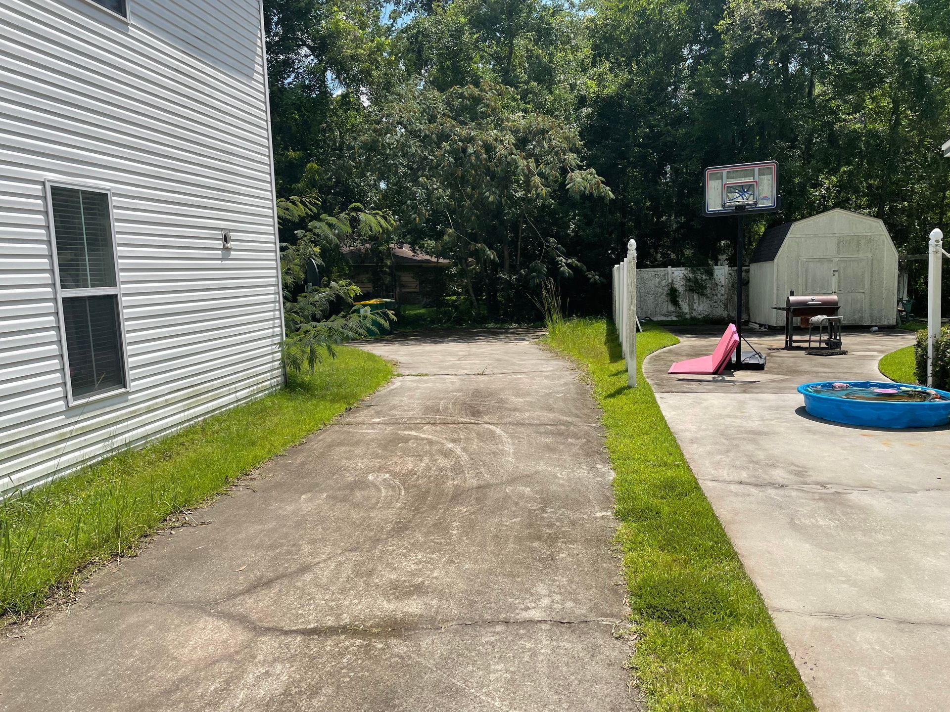 A driveway leading to a house with a basketball hoop in the backyard.